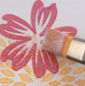 paint brush with glue on it laying on top of a pink paper flower